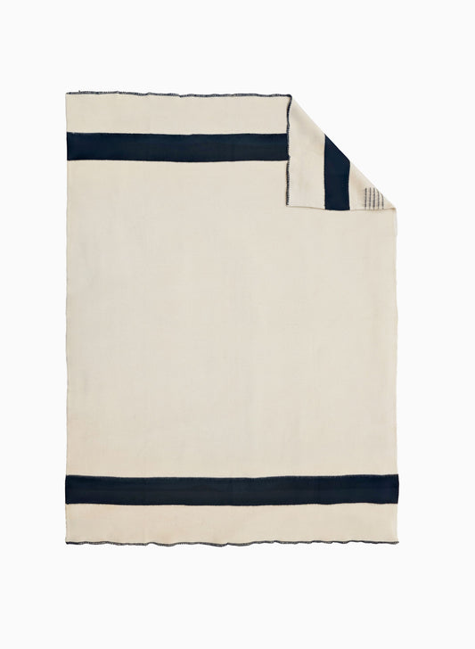 An off-white woven blanket with two thick black horizontal stripes, shown flat, with one corner folded over.