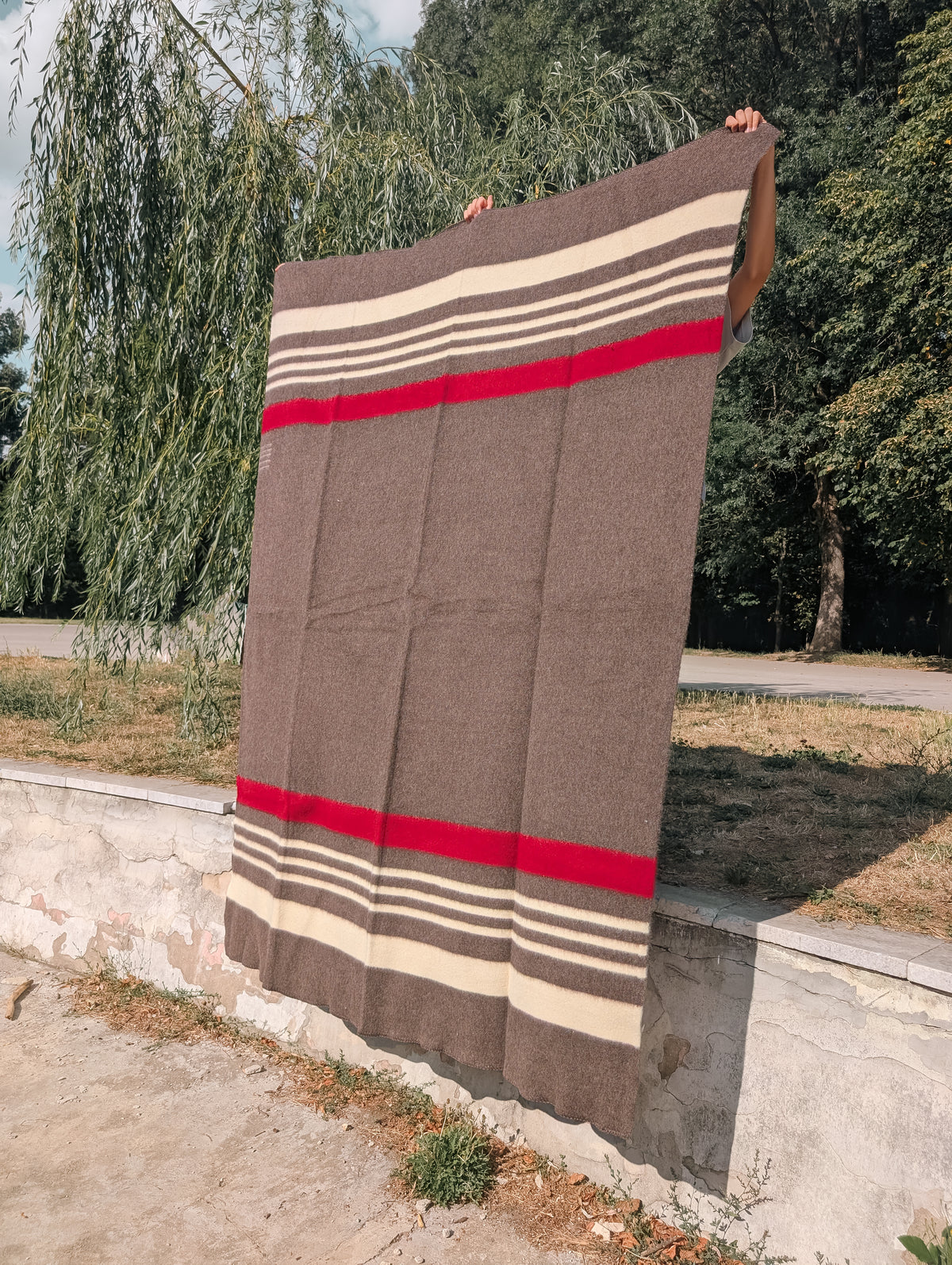 Beaver Brown 100% virgin wool blanket with red and beige stripes, held hanging outdoors