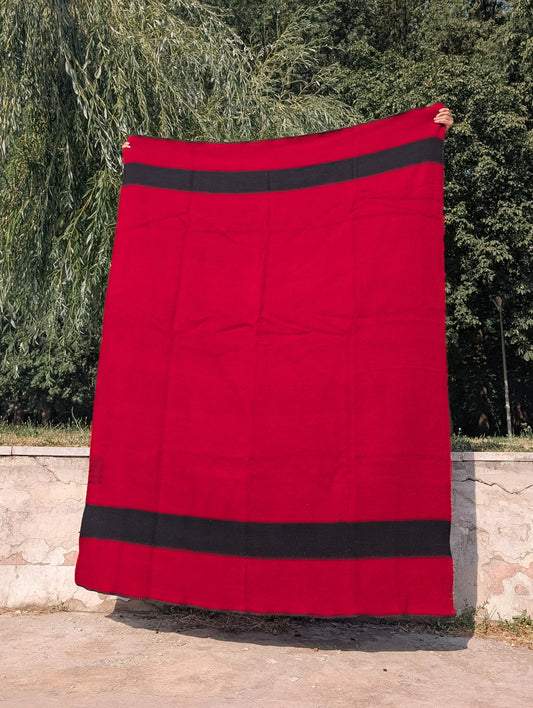 A red wool blanket with black stripes held up outdoors. Perfect for home decor, camping and reenactment.