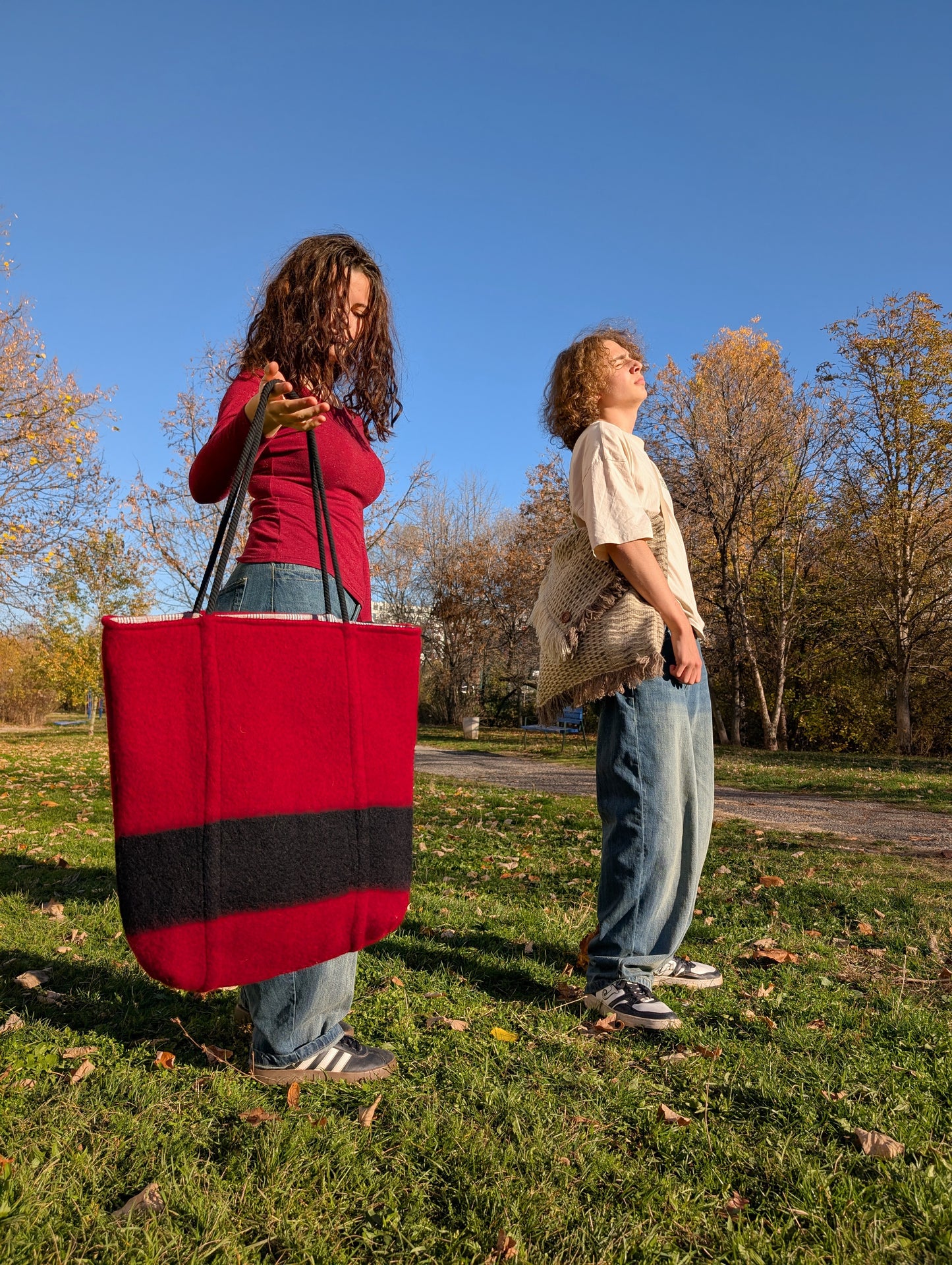 Two people standing outdoors holding handcrafted upcycled wool tote bags made from stripe blankets.