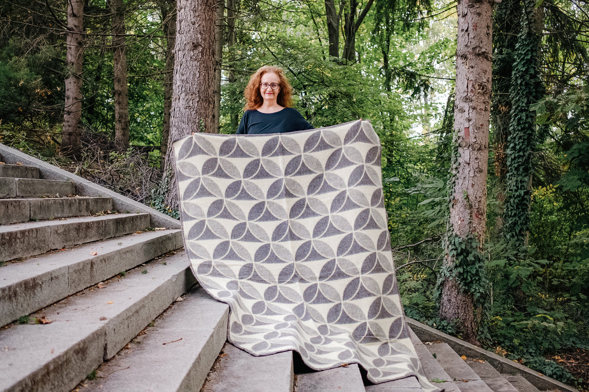 Person holding an undyed pure wool blanket in sacred geometry circle shapes with natural colors, outdoors on steps with trees in the background