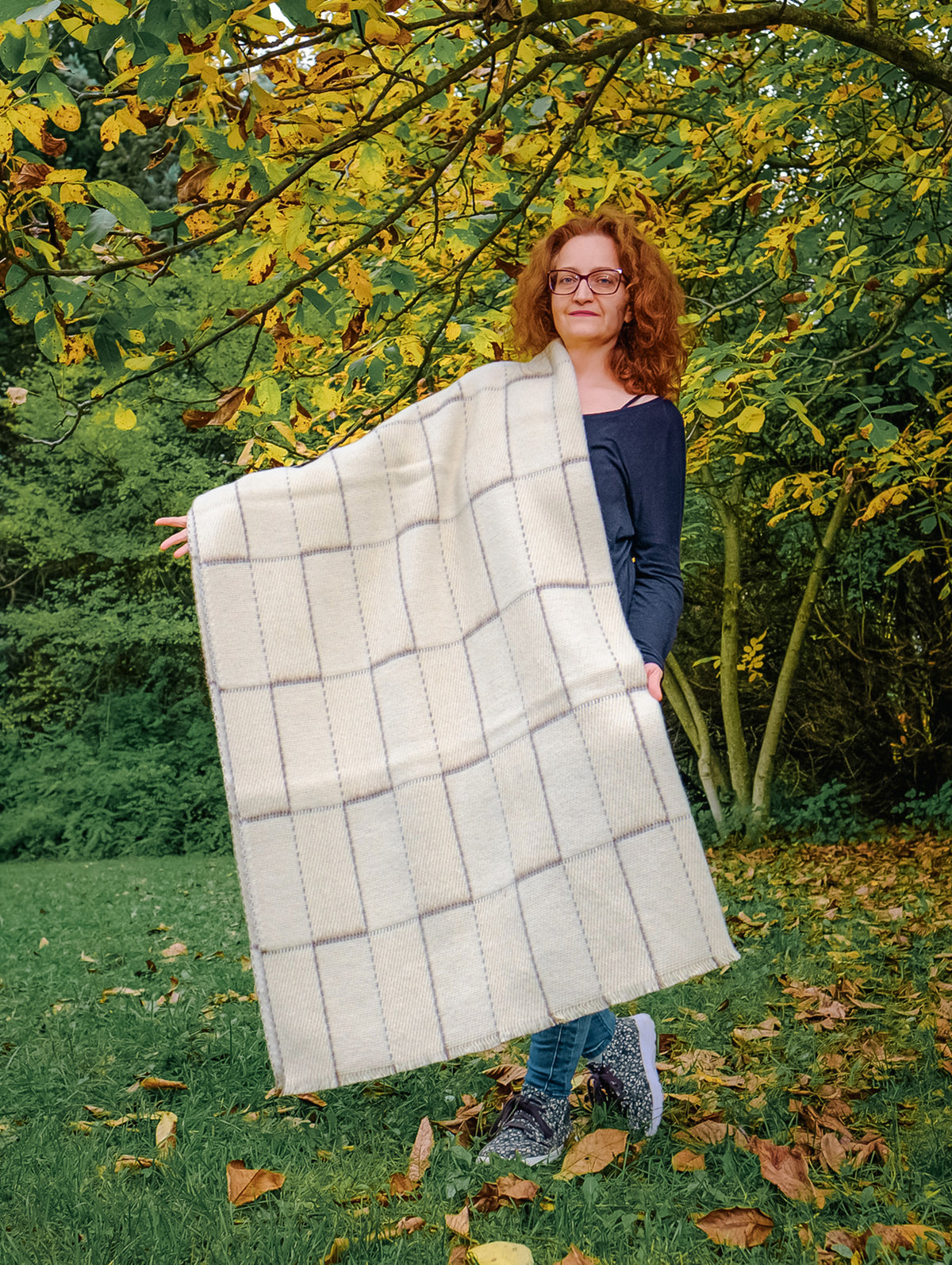 Undyed handwoven wool blanket with geometric grid pattern, shown outdoors in natural ivory wool