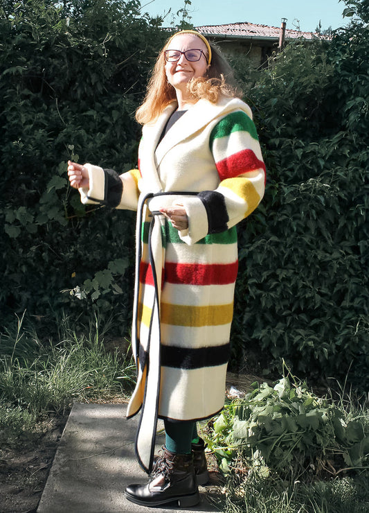 Woman wearing a colorful striped metis capote coat standing outdoors. The coat is handmade from sustainable eco wool blanket.