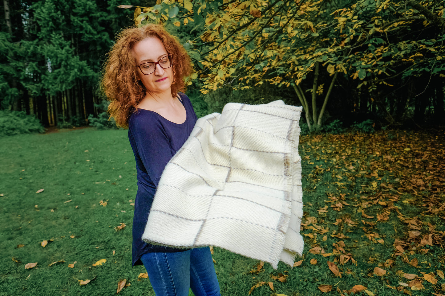Woman holding a white woven blanket made of undyed virgin wool outdoors in a garden setting.