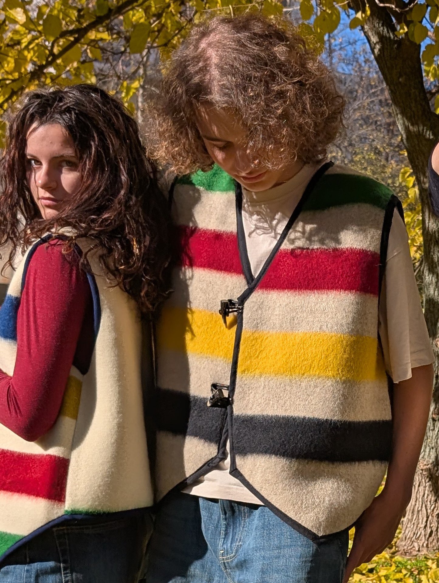 Two people wearing colorful striped vests in a natural setting with trees and leaves.