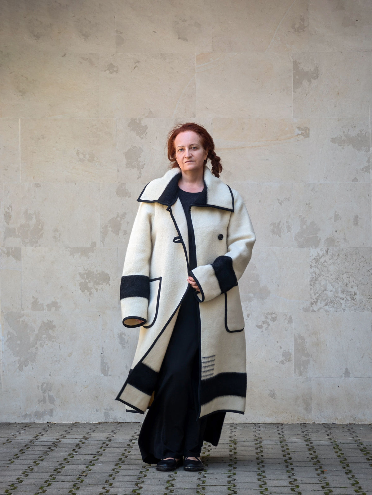 Woman wearing a long cream collar coat with black stripes, and a wide lapel, made from authentic luxurious wool blanket.