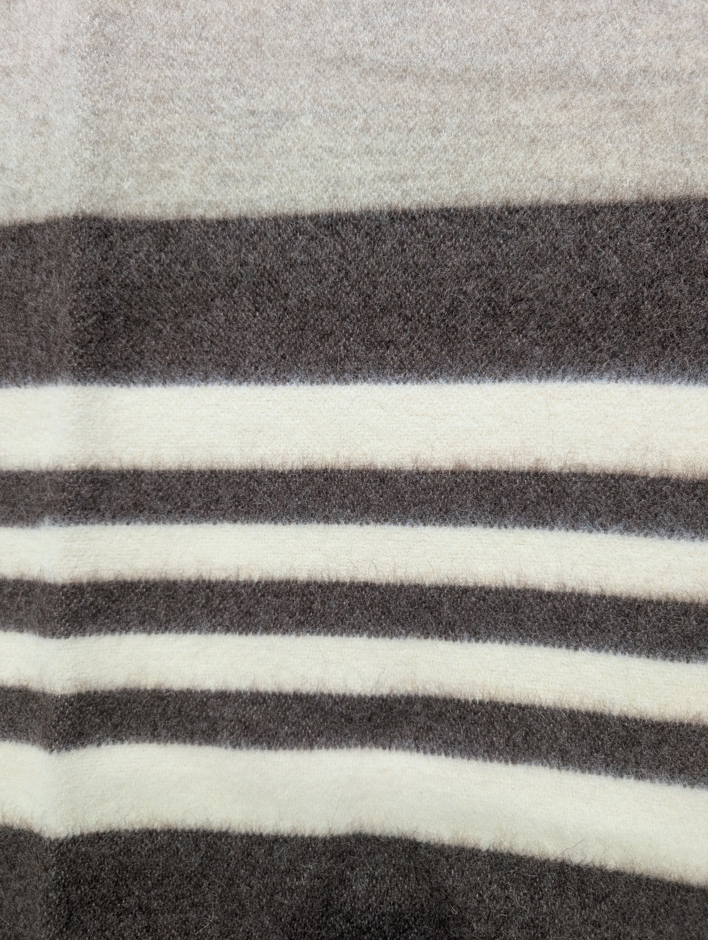 A detail of a minimalist gray wool blanket with beige and brown stripes. Undyed virgin sheep's wool handmade product.
