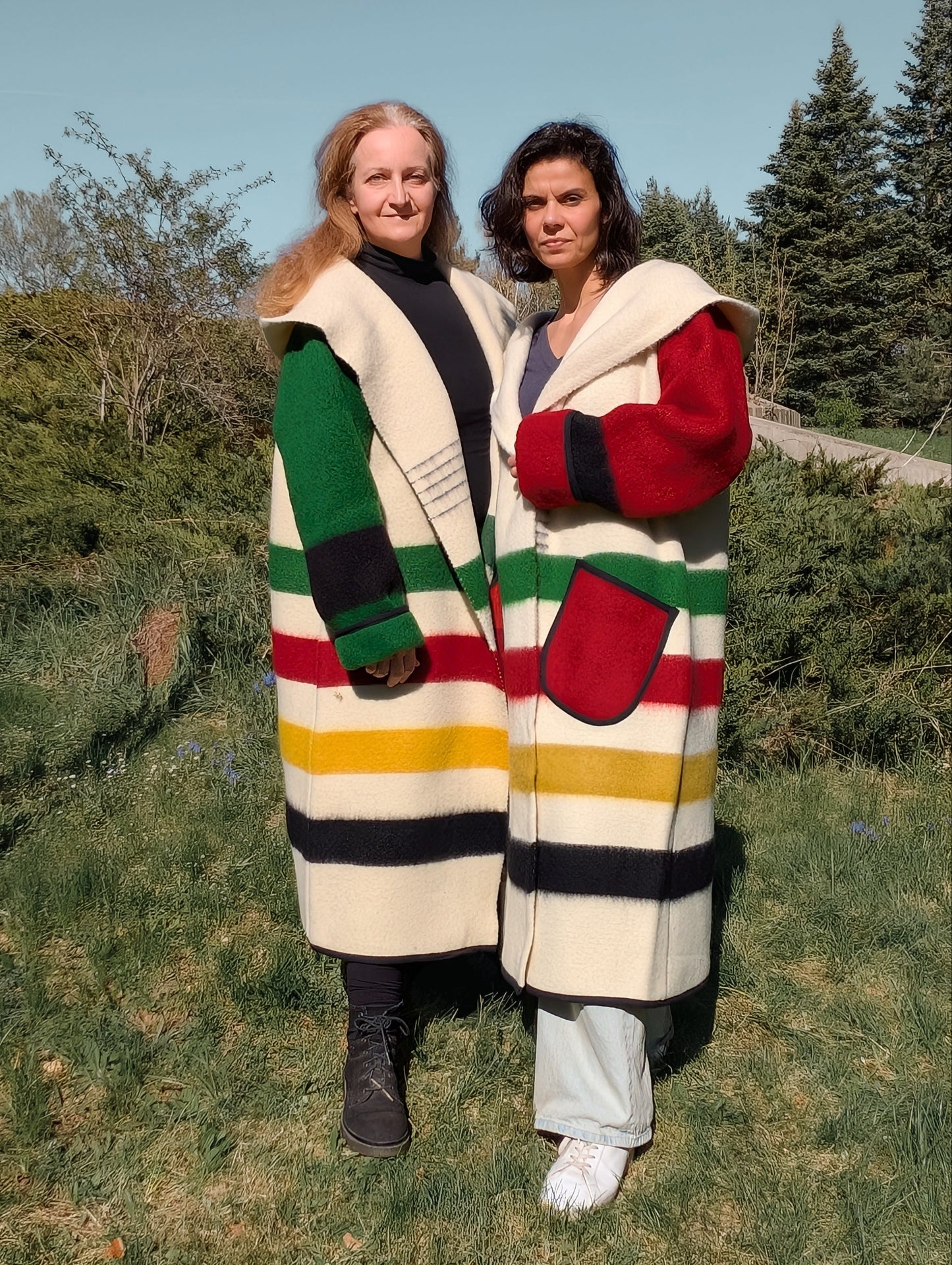 Two women wearing oversized unisex blanket overcoats with stripes distinctive colorful sleeves.
