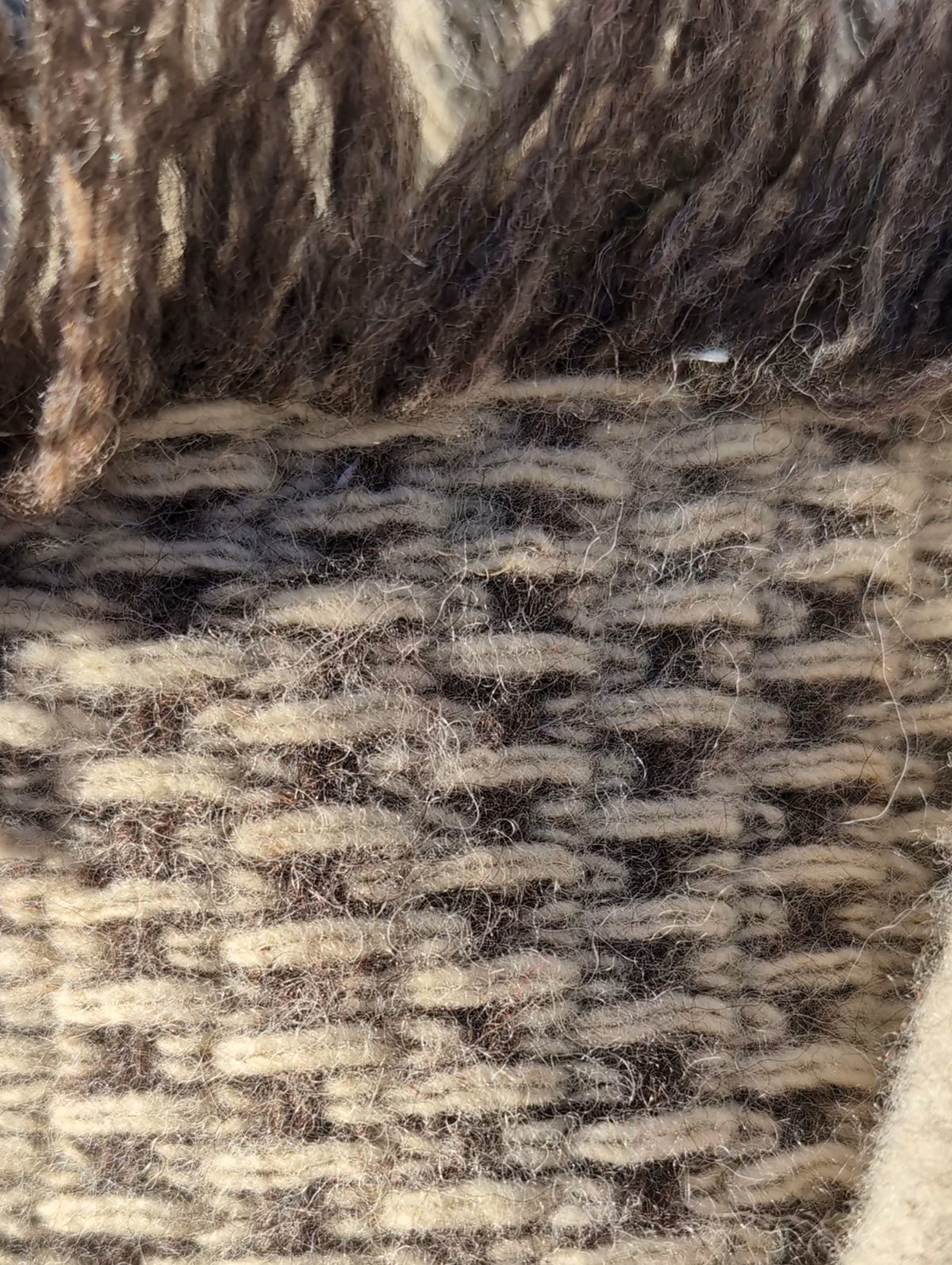 Close-up of handwoven wool undyed blanket in natural taupe and cream colors, with fringes.