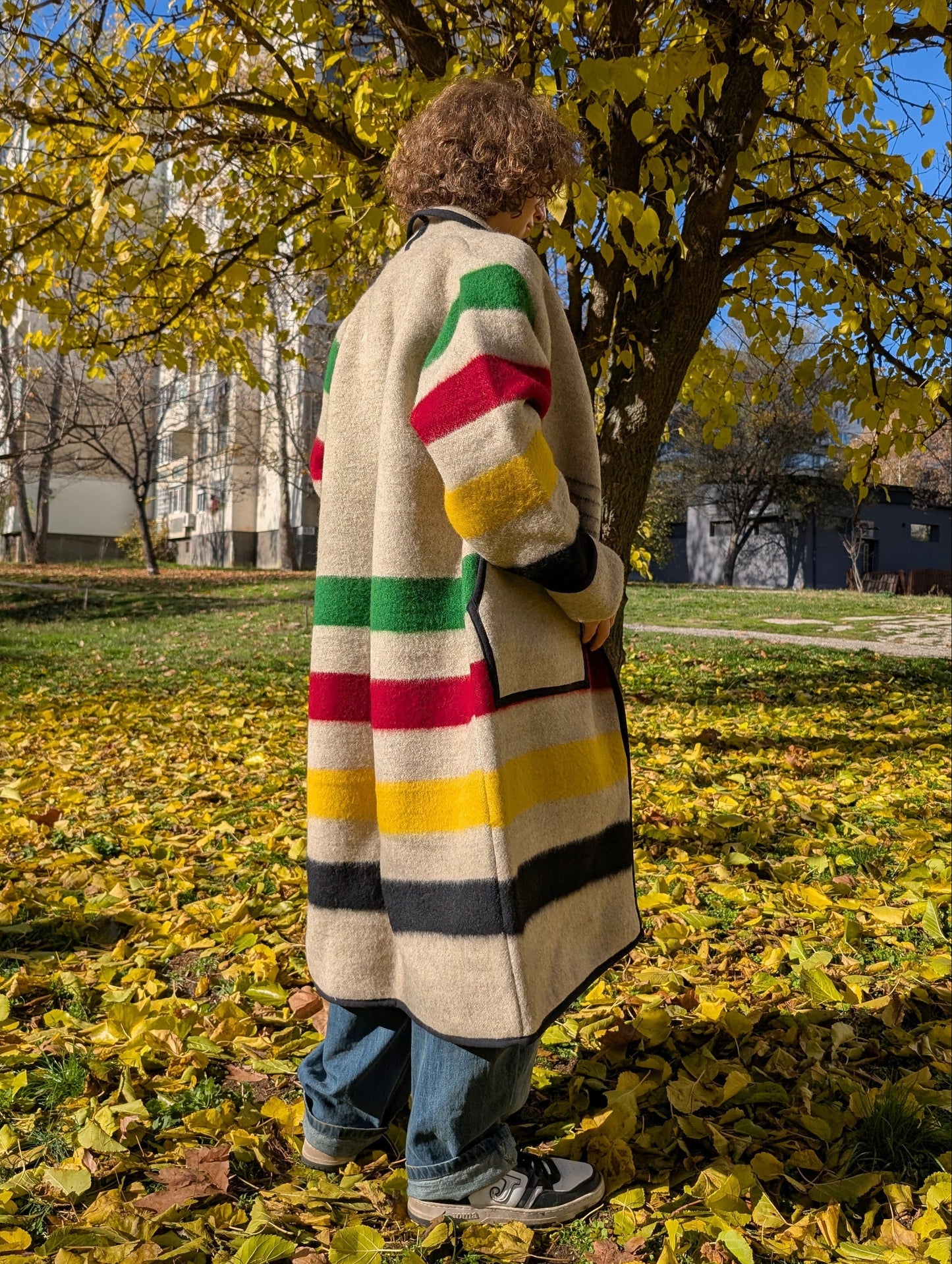 A young man wearing a long gray multi stripe blanket cardigan coat.