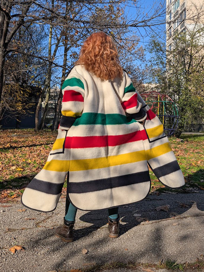 Woman wearing a loose long wrap duster coat with multistripe pattern, made from recycled handspun wool blanket.