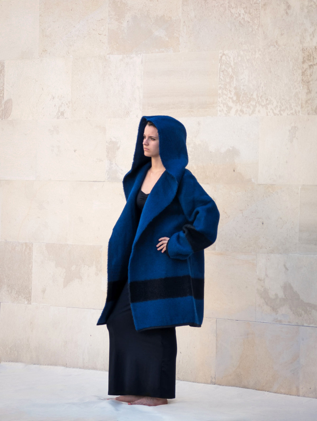 A woman wearing a modern minimalistic  hooded blanket coat in navy blue. 
