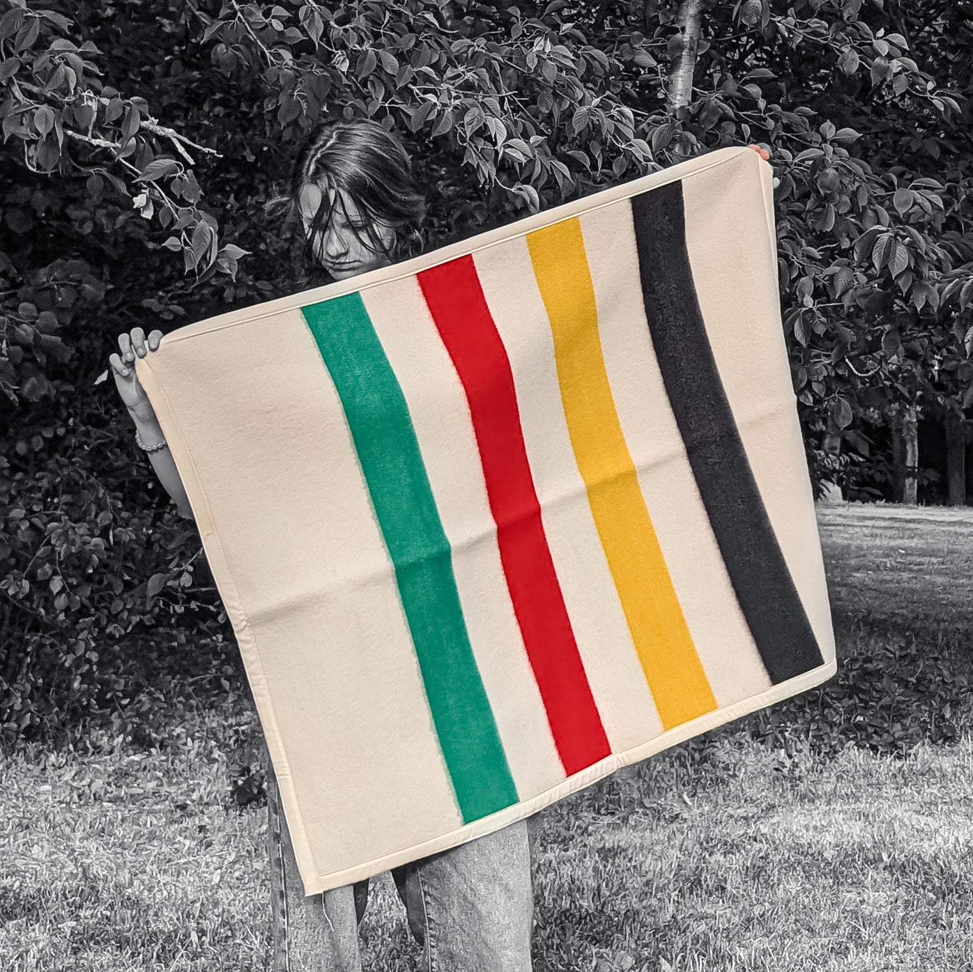 A young woman holding draped a soft baby blanket upcycled from premium wool striped blanket.