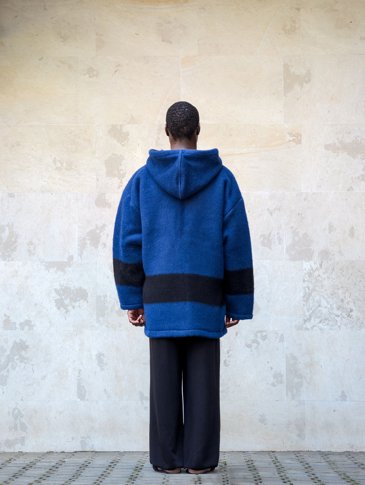 Back view of an oversized royal blue  virgin wool blanket pullover with black stripes.