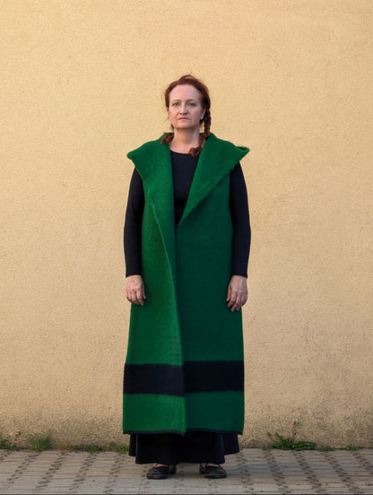 A model wearing a long green handwoven wool vest with an open front and black hem stripe.