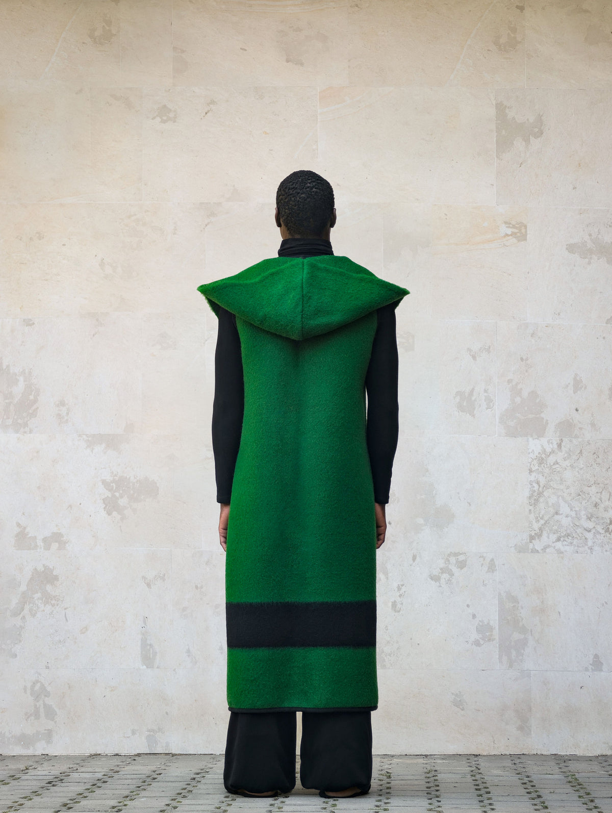 A person viewed from behind wearing a long sleeveless hooded coat 