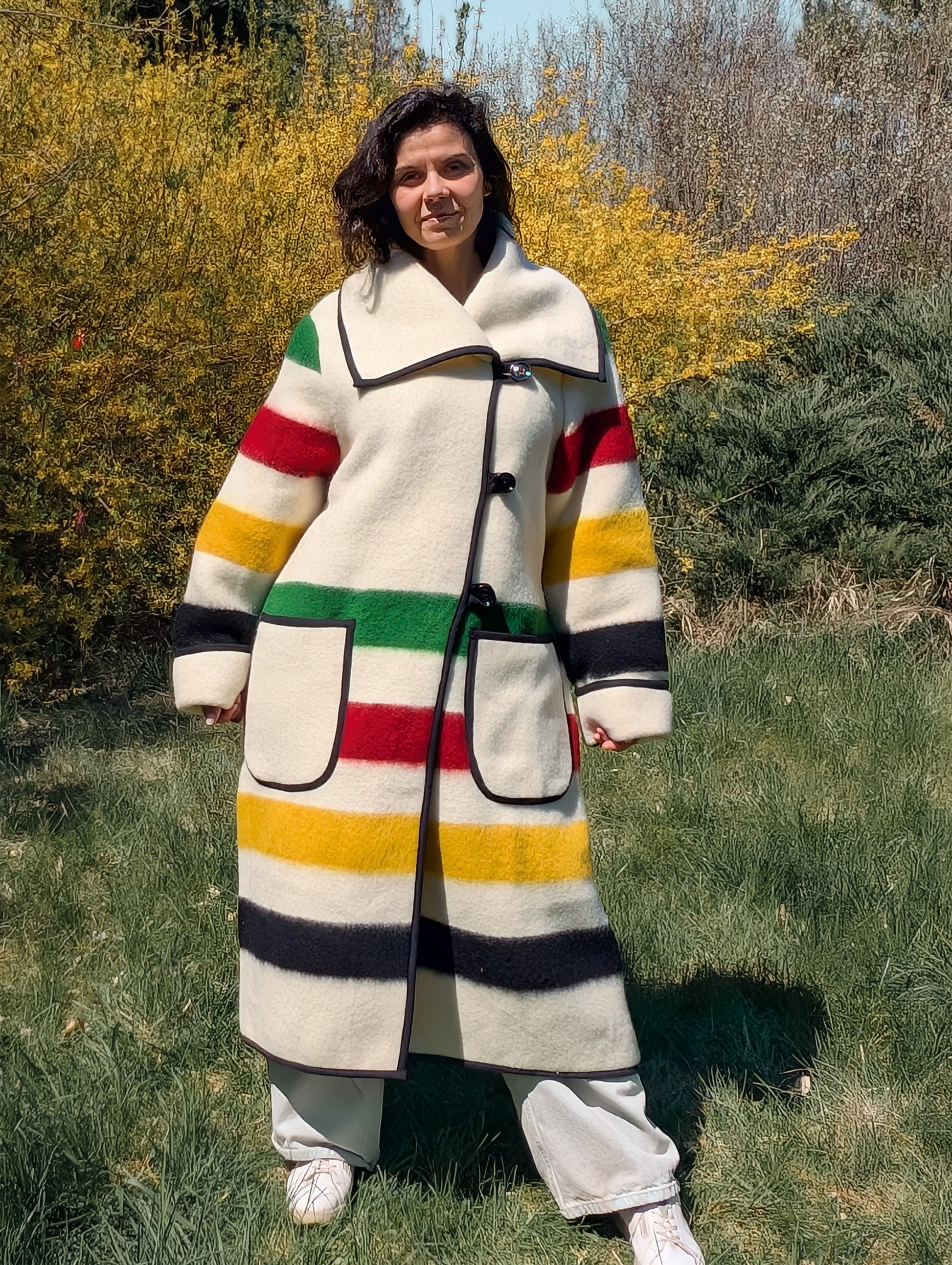 Woman wearing a long wide lapel coat with toggle button closure and 2 big front pockets. Recycled pure wool blanket outerwear.