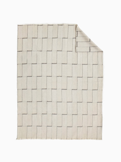 An undyed wool blanket throw in a warm cream or off-white color, with a stepped geometric grid pattern.
