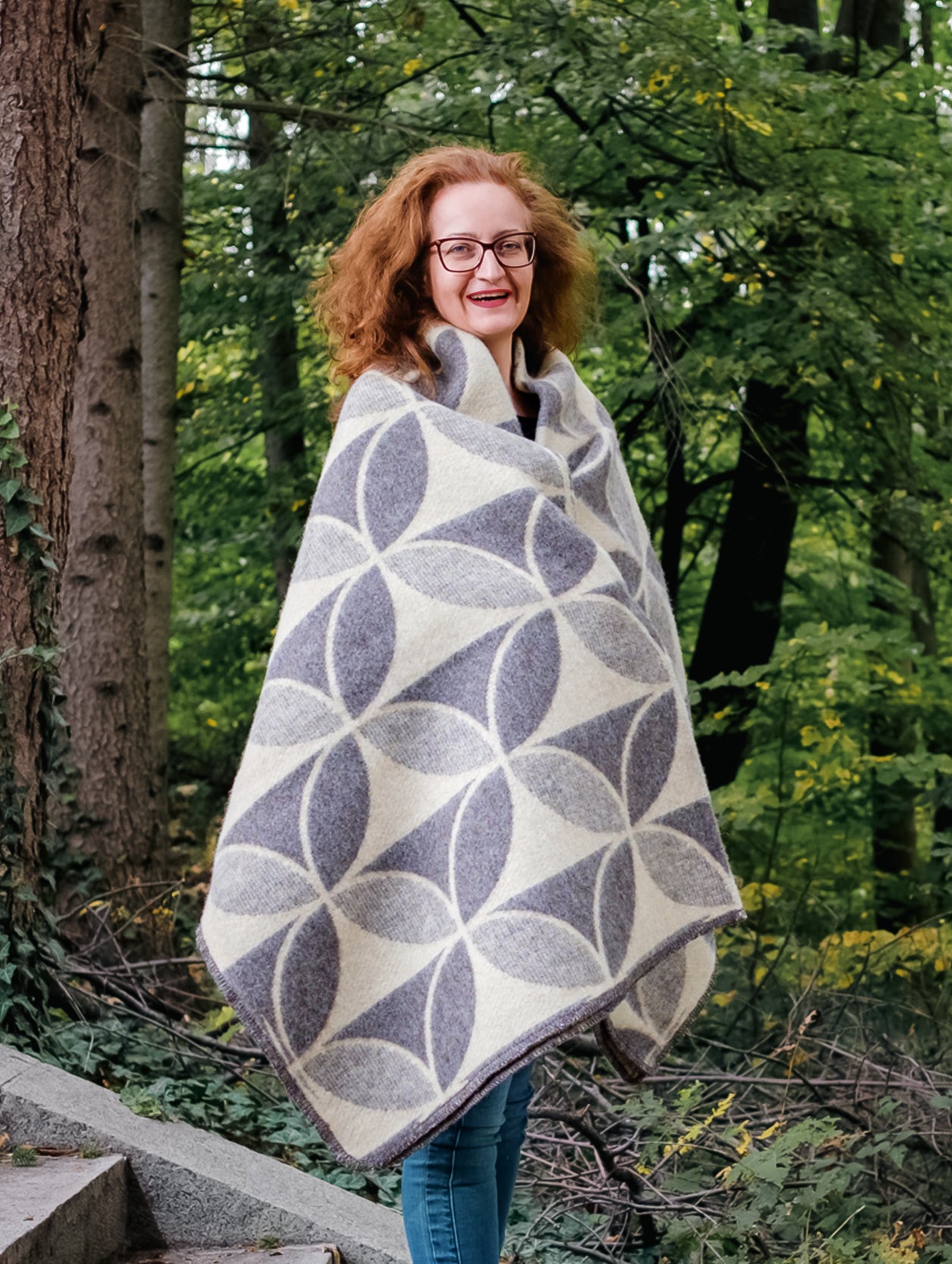 Woman standing outdoors in a forest, wrapped in a premium quality patterned pure wool blanket