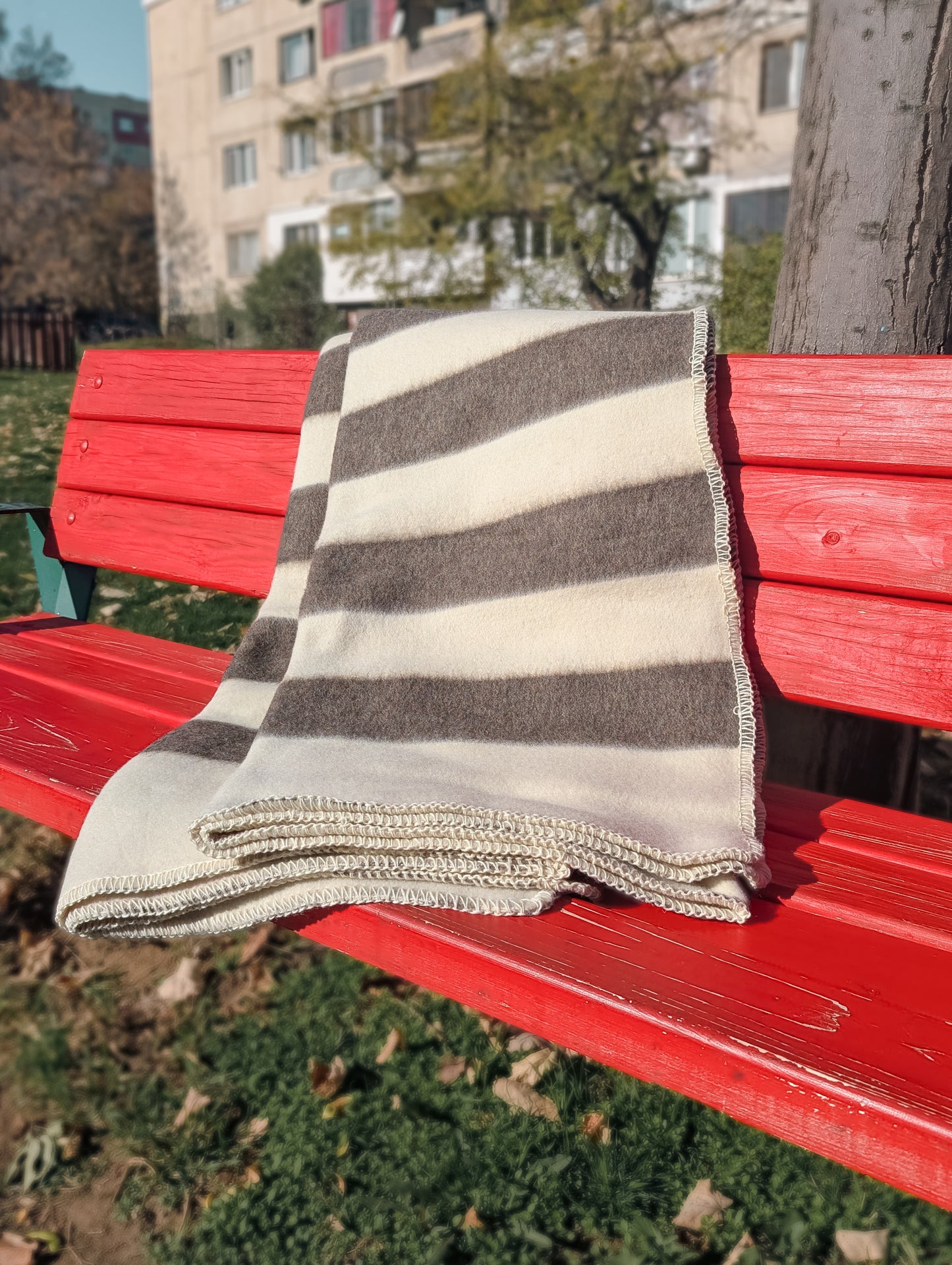 Luxurious handmade undyed wool blanket with classic stripe design in natural cream and brown tones, folded on a red bench