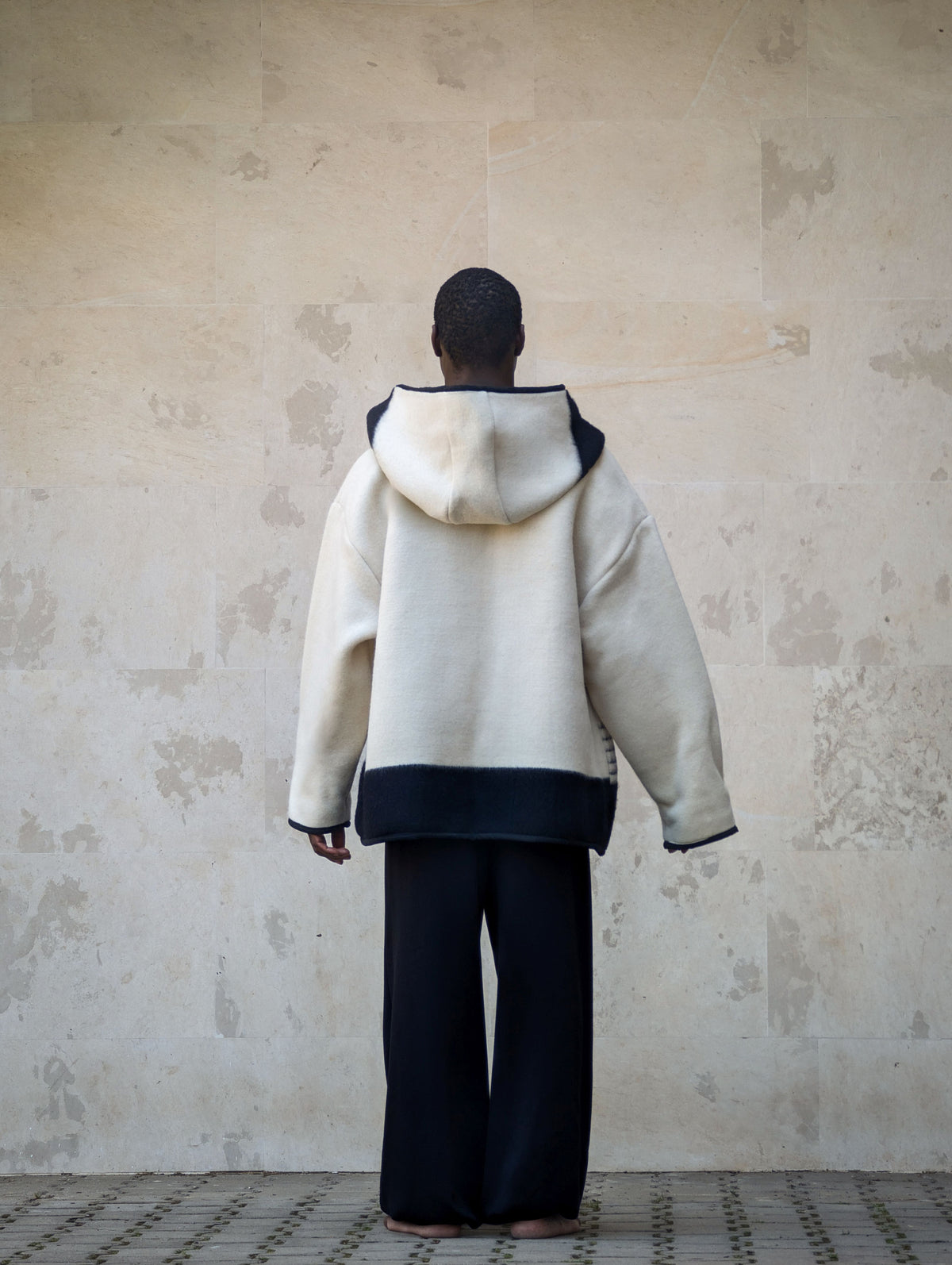 A person viewed from behind wearing an oversized cream-colored hooded jacket with black stripes. 