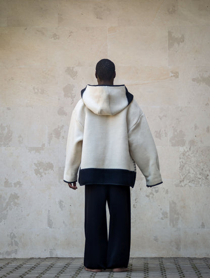 A person viewed from behind wearing an oversized cream-colored hooded jacket with black stripes. 