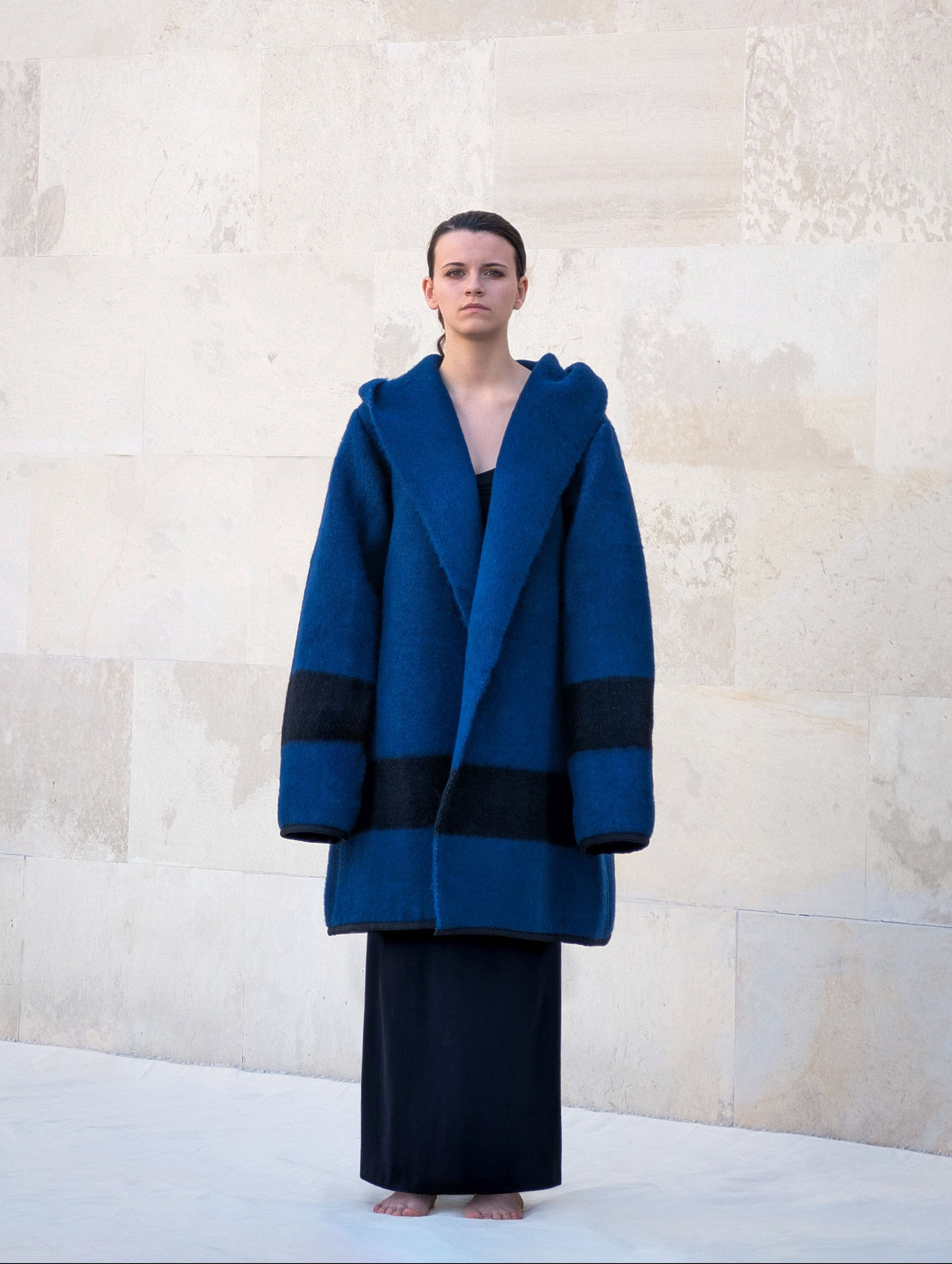 A front view of a female model wearing a custom-made wool coat with wide collar turning into a hood