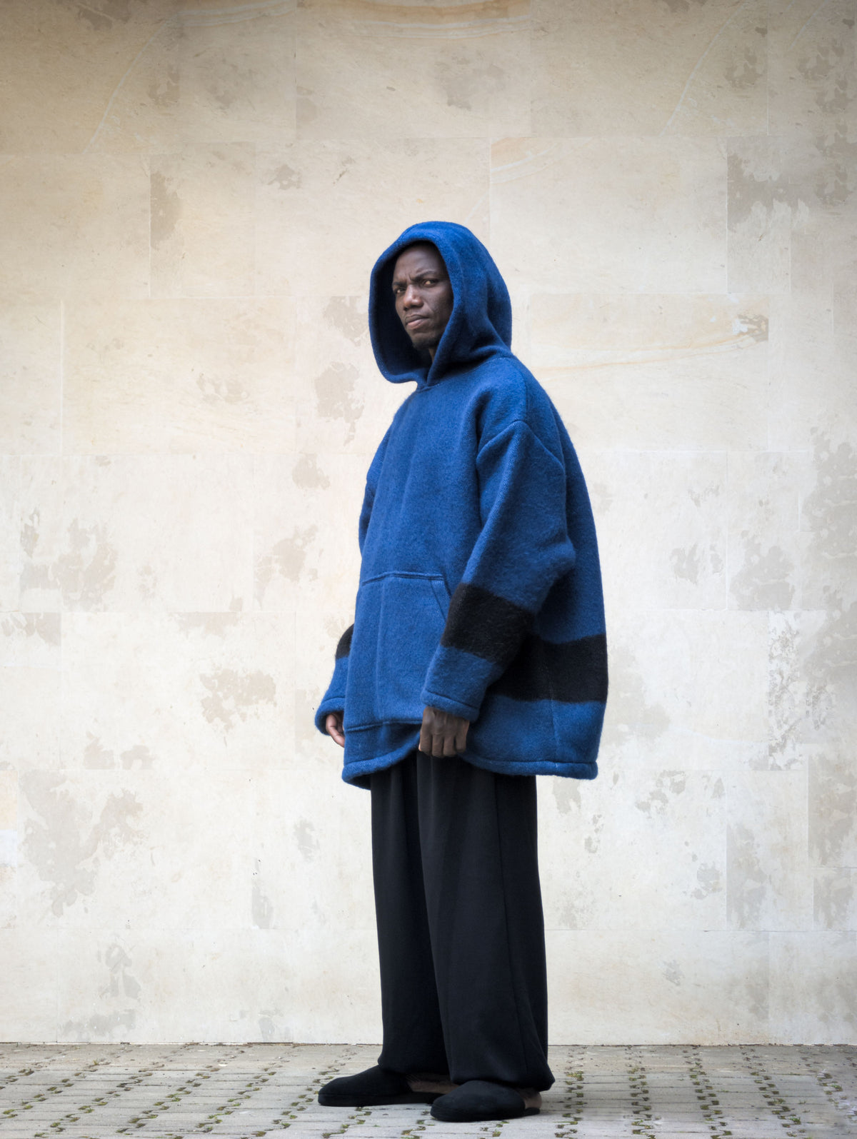 Side profile of a model wearing a heavy blue handwoven wool pullover hoodie with deep hood up.