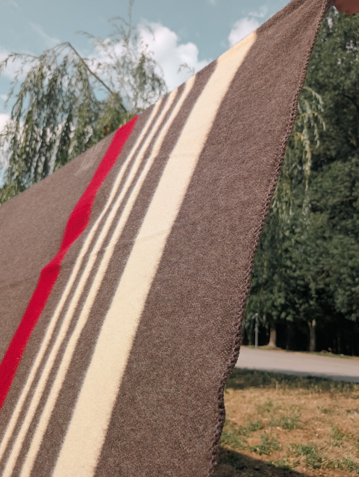 Close-up of a textured wool blanket throw with red, ecru, and brown colors against a natural background. 