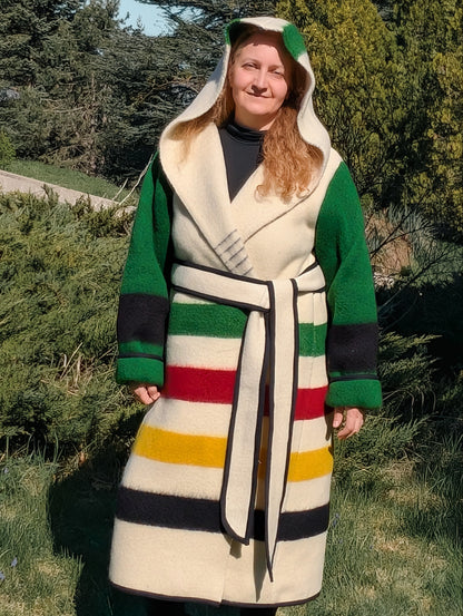 Woman wearing a long hooded capote coat with colorful stripes and green sleeves, upcycled from a single woolen blanket.