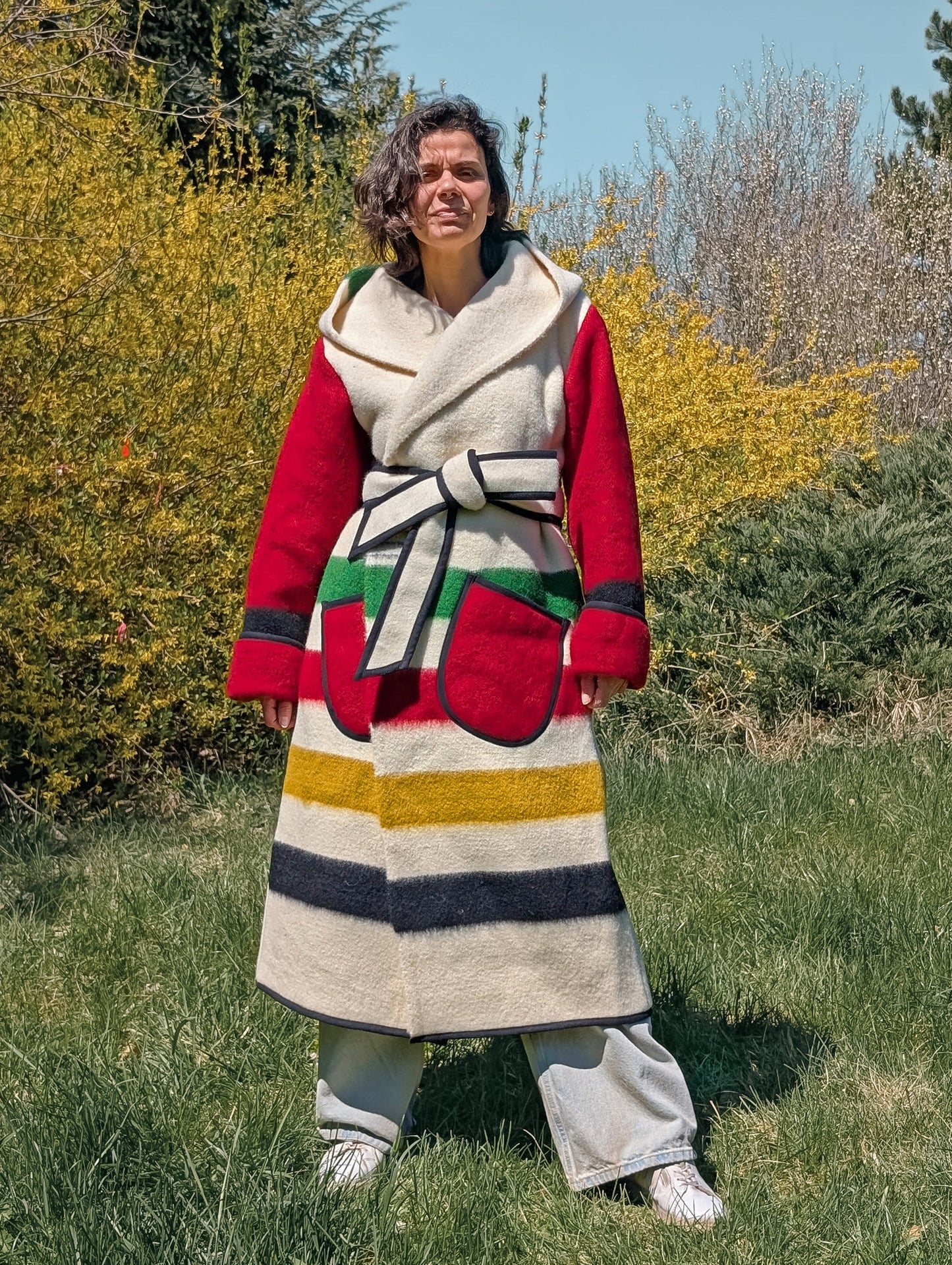 Woman dressed with a statement wrap overcoat featuring iconic stripes and red sleeves. Bespoke garment, tailored from a single stripe woolen throw.