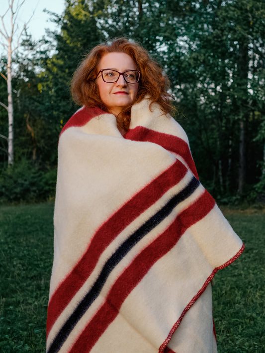 A ginger woman posing wrapped in a striped  blanket with red and black stripes in a nature park setting