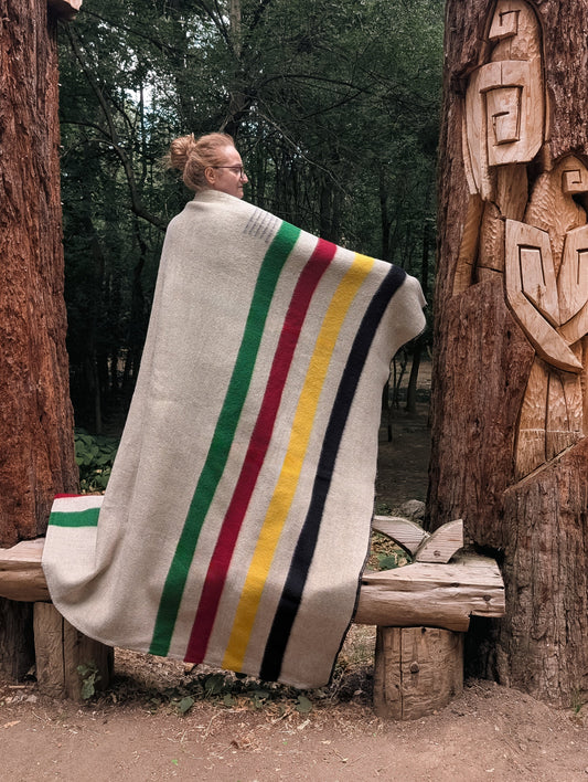A woman wrapped in premium quality gray wool  blanket accented with iconic multicolored stripes