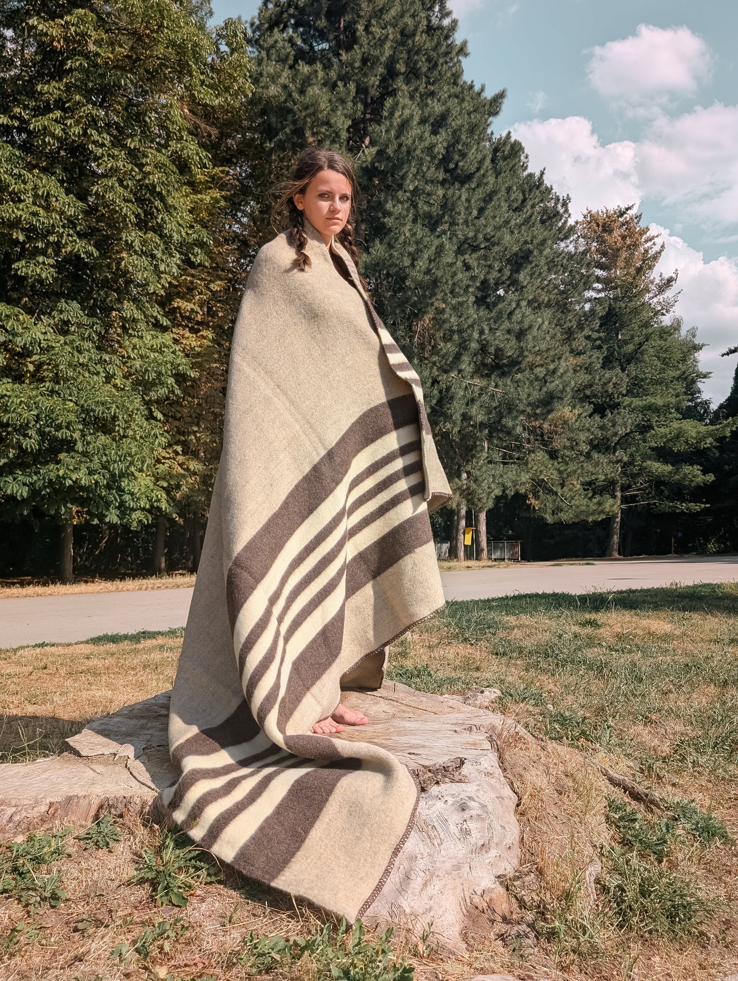 A woman wrapped in a gray wool cabin throw with white and brown stripes in an outdoor setting. Handwoven undyed natural wool throw.