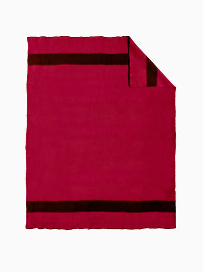 A handwoven striped wool throw blanket in solid magenta-red with black stripes, and a flipped corner. 