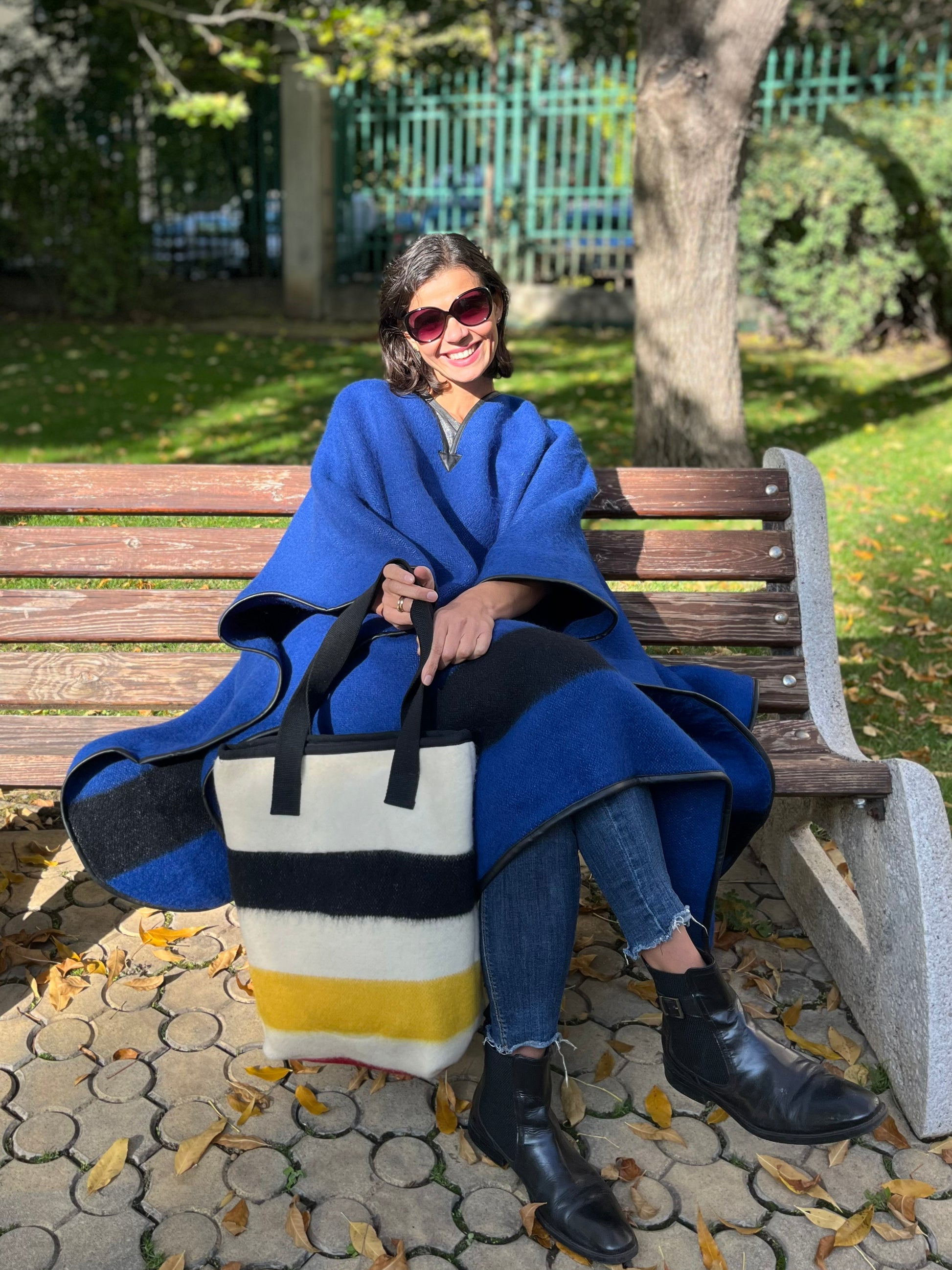 Woman in a blue coat sitting on a bench with a colorful multistriped shopping bag tailored from  authentic handwoven blanket cuts.