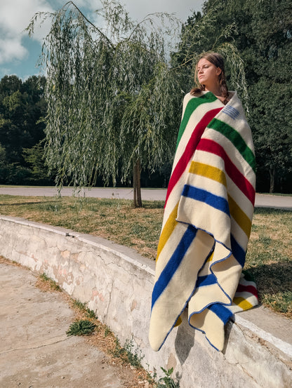 A girl wrapped in a multistripe blanket in ivory with colorful stripes, handwoven from pure wool.