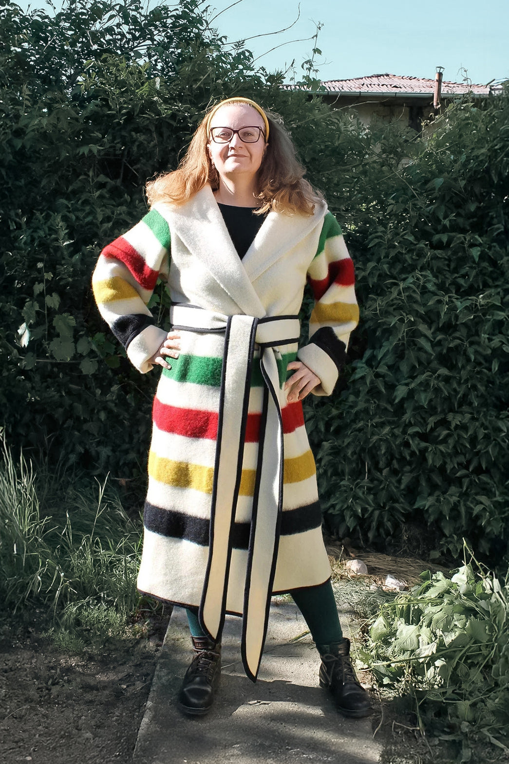 Woman wearing a colorful striped capote coat standing outdoors. The coat is handmade from sustainable eco wool  blanket.
