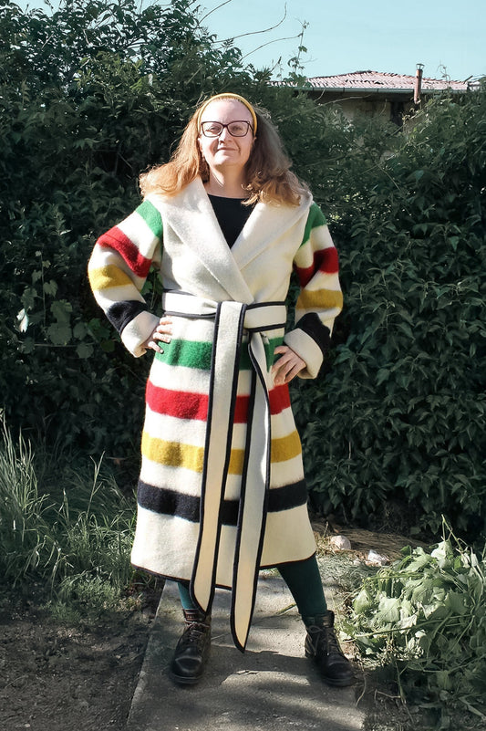 Woman wearing a colorful striped capote coat standing outdoors. The coat is handmade from sustainable eco wool  blanket.