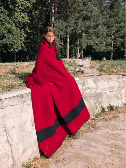 Person covered with a Heritage red wool blanket, with a black stripe.
