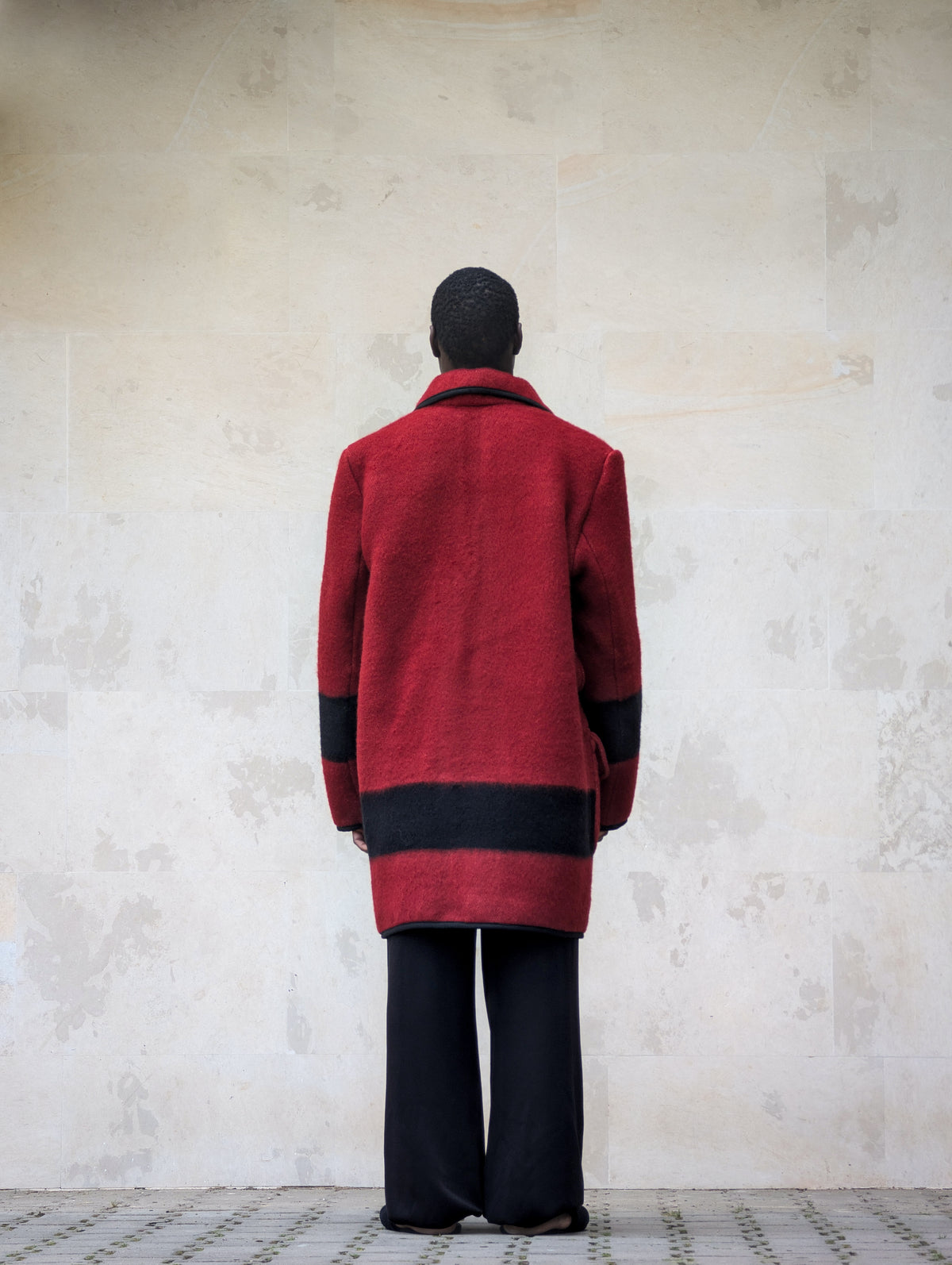 Back view of a red handwoven pure wool blanket coat featuring a wide black horizontal stripe
