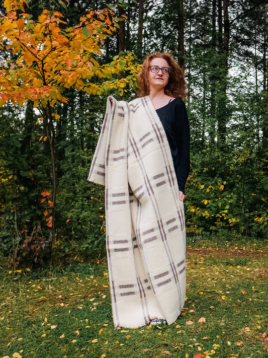 Woman holding a large undyed wool throw with minimalistic geometric design and natural earth tones