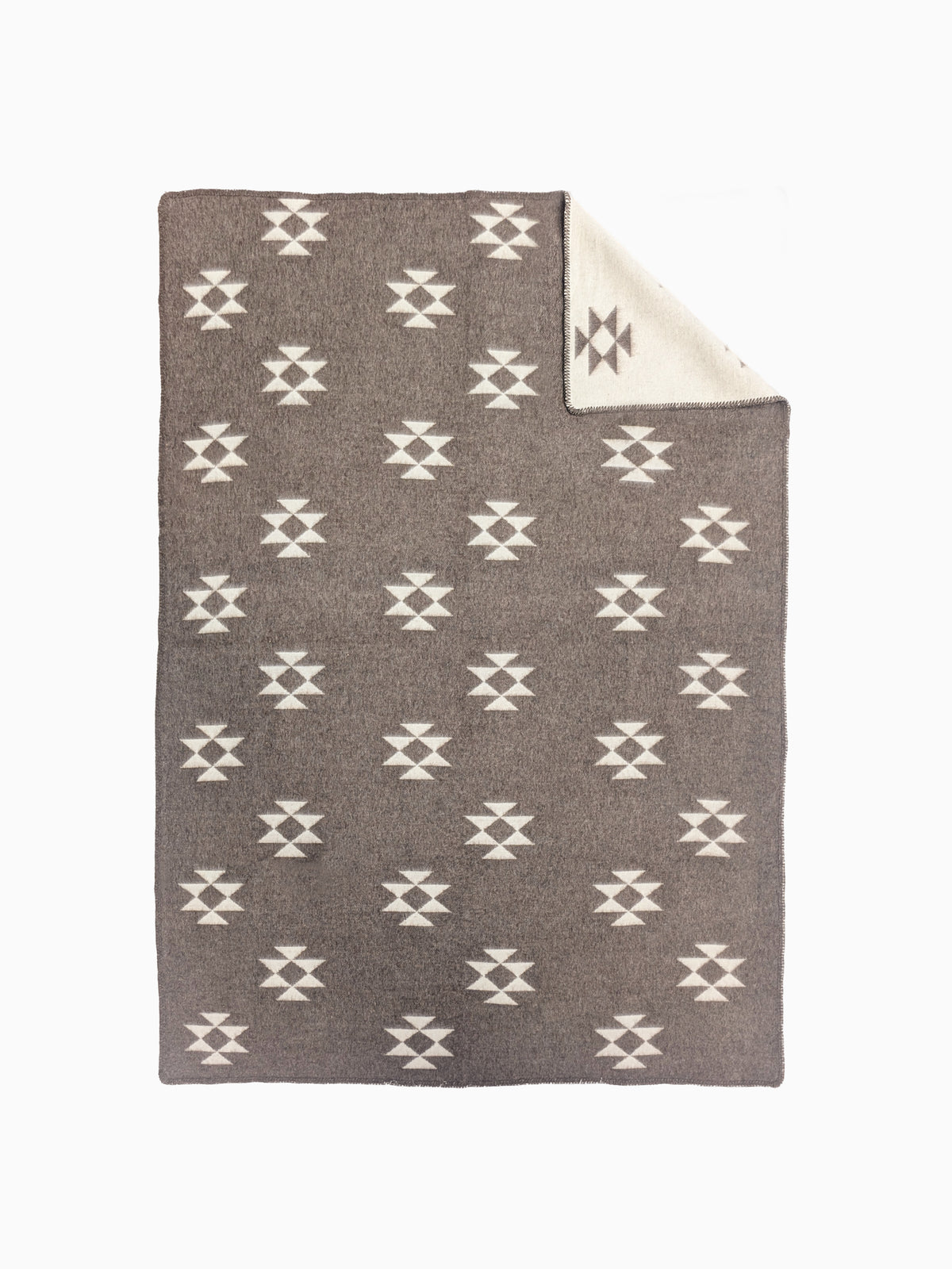 A handmade woven throw blanket with a repeating white geometric star pattern on a taupe-brown background, featuring a folded corner that reveals a cream-colored reverse side