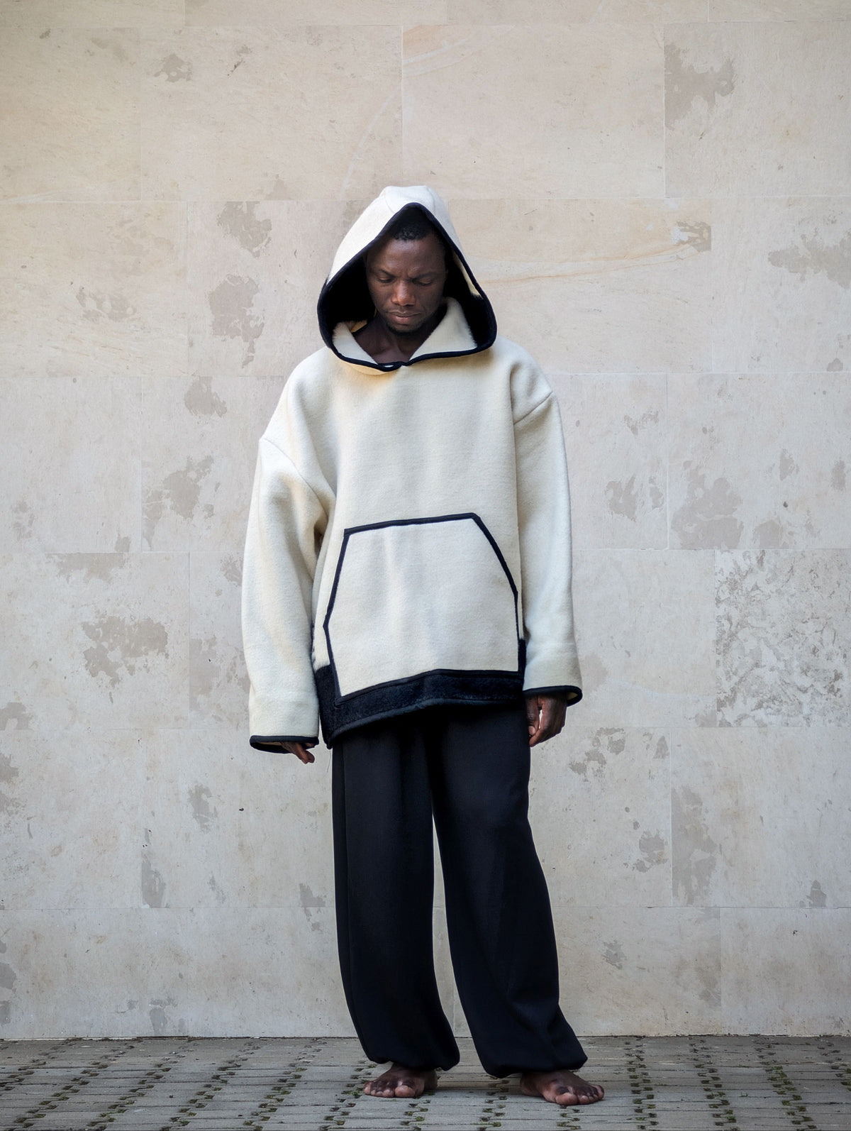 A person wearing a cream-colored oversized hooded sweatshirt with black stripe at the bottom and a generos hood. 
