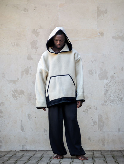 A person wearing a cream-colored oversized hooded sweatshirt with black stripe at the bottom and a generos hood. 