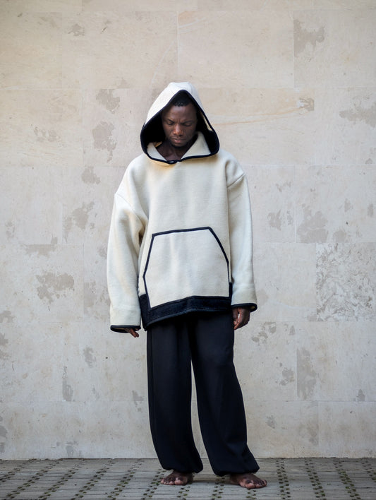 A person wearing a cream-colored oversized hooded sweatshirt with black stripe at the bottom and a generos hood. 