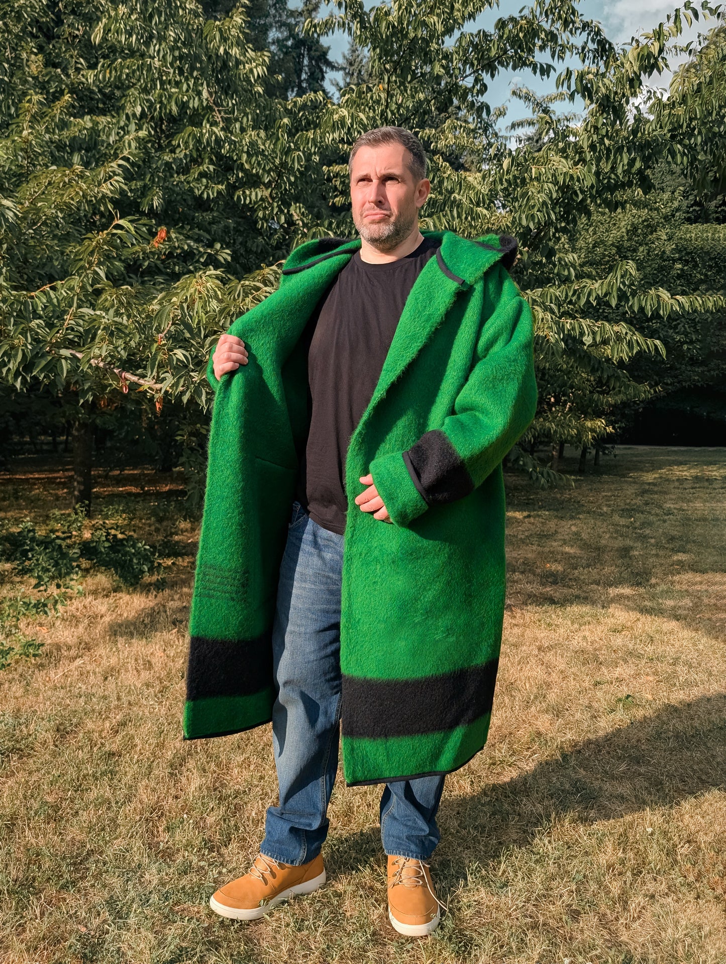 Man wearing a long robe capote coat or wrap coat in solid green with a black stripe, all upcycled from a native organic wool blanket.