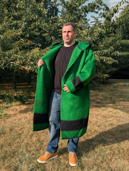 Man wearing a long robe capote coat or wrap coat in solid green with a black stripe, all upcycled from a native organic wool blanket.