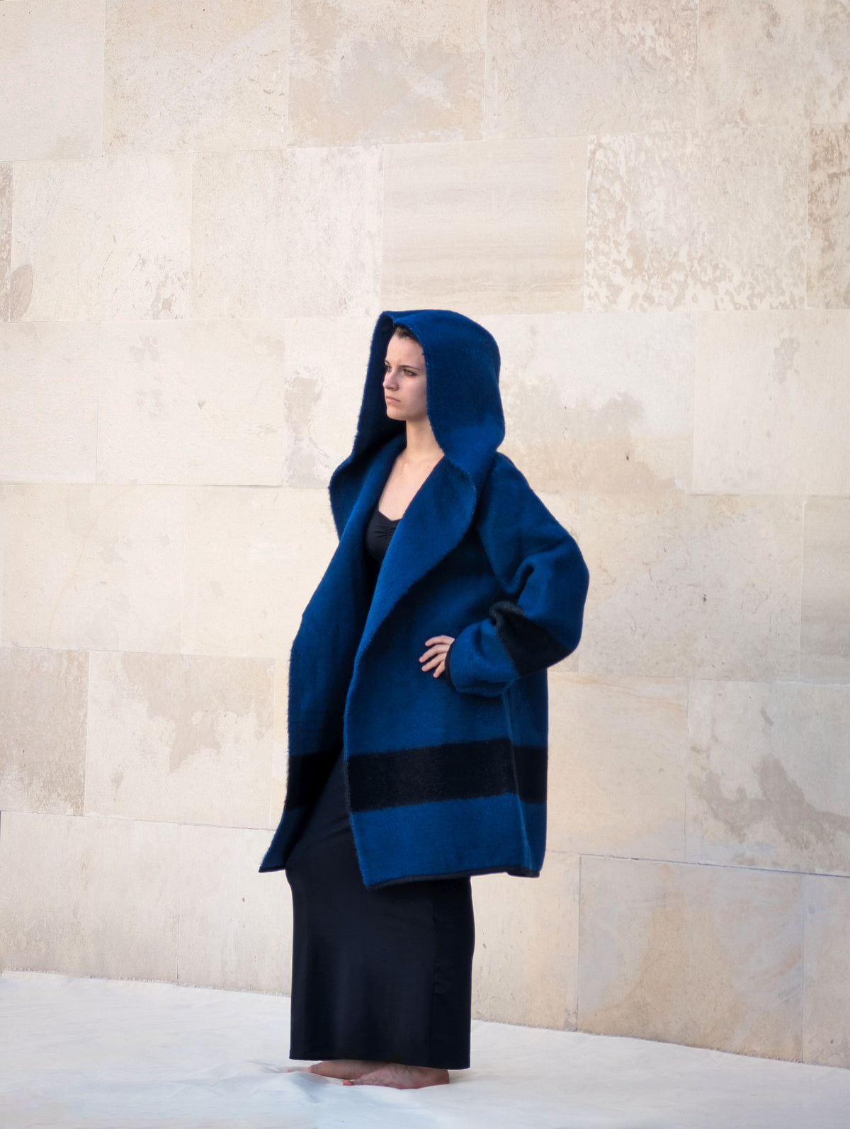 A woman wearing a modern minimalistic  hooded blanket coat in navy blue. 