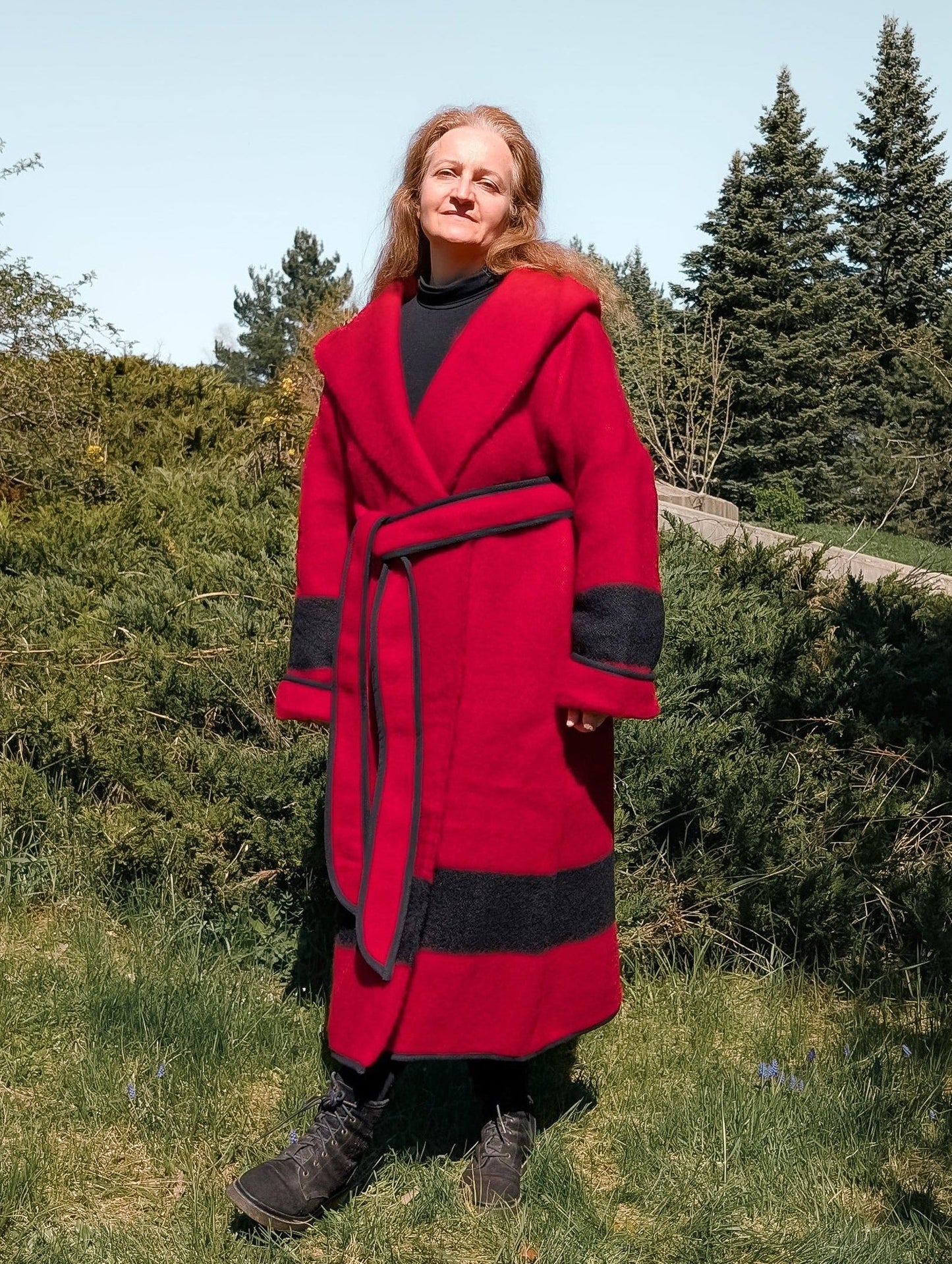 A woman wearing a pure wool capote coat in solid red with a black stripe, upcycled from a single wool blanket.